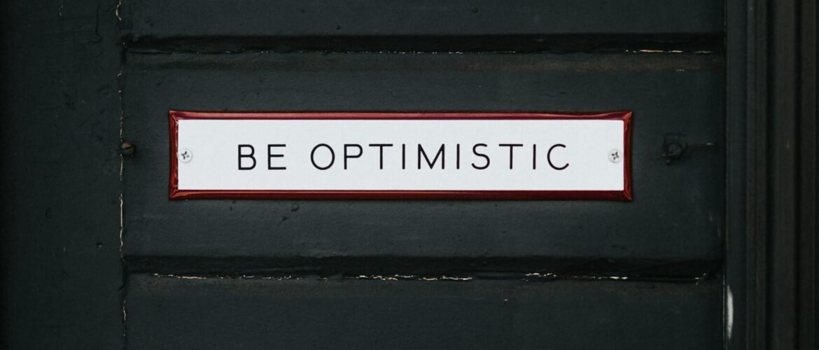 black wooden door with be optimistic text overlay