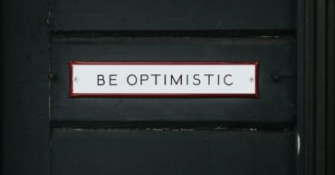 black wooden door with be optimistic text overlay